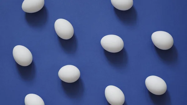 Pattern with white eggs on blue background. Eggs in minimal flat lay style — Φωτογραφία Αρχείου