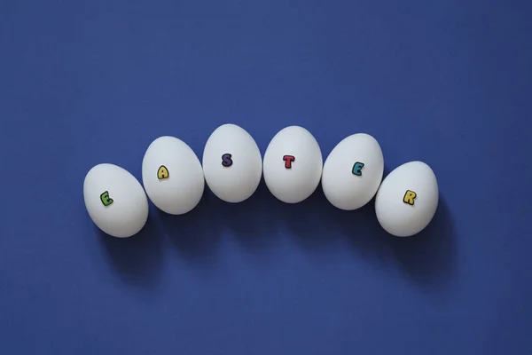 Creative layout of white chicken eggs with the inscription Easter from colored letters on a blue background. — Φωτογραφία Αρχείου