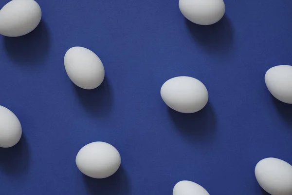 Візерунок з білими яйцями на синьому фоні. Яйця в мінімальному стилі плоского шару — стокове фото