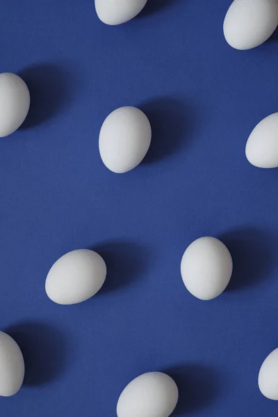 Візерунок з білими яйцями на синьому фоні. Яйця в мінімальному стилі плоского шару — стокове фото