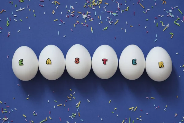 Творче компонування білих курячих яєць з написом Великдень з кольорових літер на синьому фоні . — стокове фото