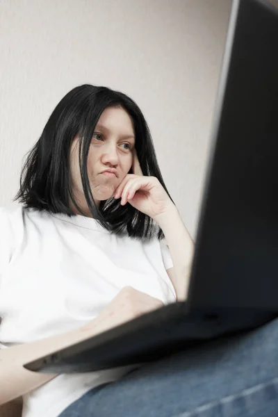 Mujer joven disgustada trabaja desde casa mientras está sentada en un sofá . — Foto de Stock