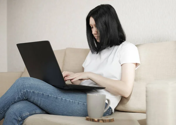 Een jonge vrouw werkt vanuit huis terwijl ze op een bank zit. — Stockfoto