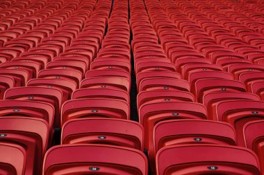 Boş bir stadyumda boş kırmızı plastik koltuklar. Tribünlerde seyirciler için bir sürü boş koltuk var. Futbol taraftarları için boş plastik sandalyeler.