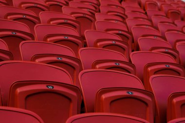 Boş bir stadyumda boş kırmızı plastik koltuklar. Tribünlerde seyirciler için bir sürü boş koltuk var. Futbol taraftarları için boş plastik sandalyeler.