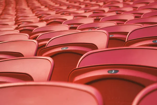 Empty red plastic seats in an empty stadium. Many empty seats for spectators in the stands. Empty plastic chairs seats for football fans.