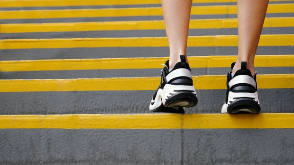 Close-up of sneakers on female legs on the stairs in the stadium, rear view. Female muscular legs in sneakers. Concepts of sport, health and wellness.