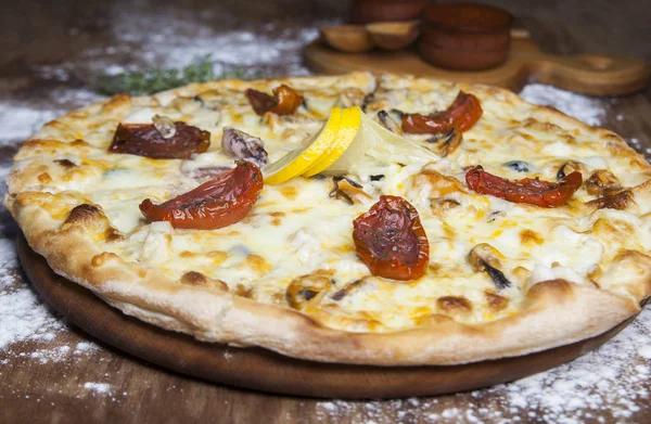 Pizza met kaas zongedroogde tomaten zeevruchten en citroen — Stockfoto