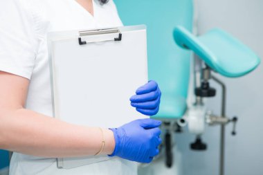 Beyaz önlüklü ve mavi steril eldivenli bir jinekolog hastanın tıbbi geçmişinin boş formlarını tutuyor. Üreme tıbbı