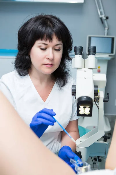 Siyah saçlı, beyaz önlüklü ve mavi steril eldivenli bir jinekolog jinekolojik aynalı ve genişleticili bir hastayı muayene ediyor.