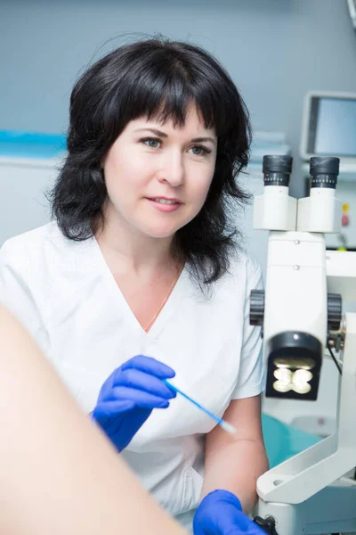 Siyah saçlı, beyaz önlüklü ve mavi steril eldivenli bir jinekolog jinekolojik aynalı ve genişleticili bir hastayı muayene ediyor.