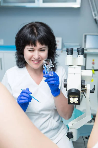 Siyah saçlı, beyaz önlüklü ve mavi steril eldivenli bir jinekolog jinekolojik aynalı ve genişleticili bir hastayı muayene ediyor.