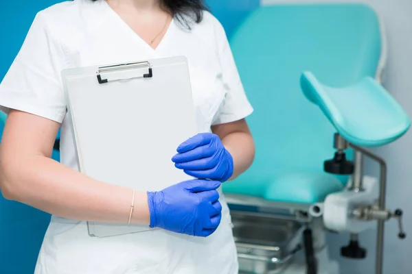Beyaz önlüklü ve mavi steril eldivenli bir jinekolog hastanın tıbbi geçmişinin boş formlarını tutuyor. Üreme tıbbı