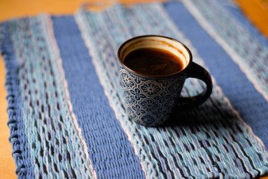 Farklı mavi renklerde el dokuması masa örtüsü. Üstte duran bir fincan kahve. Metin uzayı.