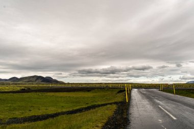 İzlanda 'daki lav tarlasını geçen düz bir yol. Arkaplanda kara bulutlar ve dağ
