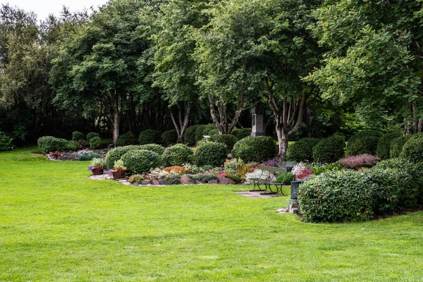 A garden landscape design featuring lawns, trees, evergreen topiary bushes and flower bed