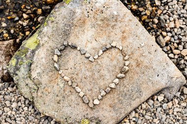 Sol üst tarafında yeşil yosunlarla kaplı düz taşın üzerindeki küçük çakıl taşlarından yapılmış kalp şekli. Farklı kesimlerdeki çakıl taşlarıyla çevrili. Taş kalpli yassı kadın. Taş dokusu. Yatay olarak. Üst görünüm