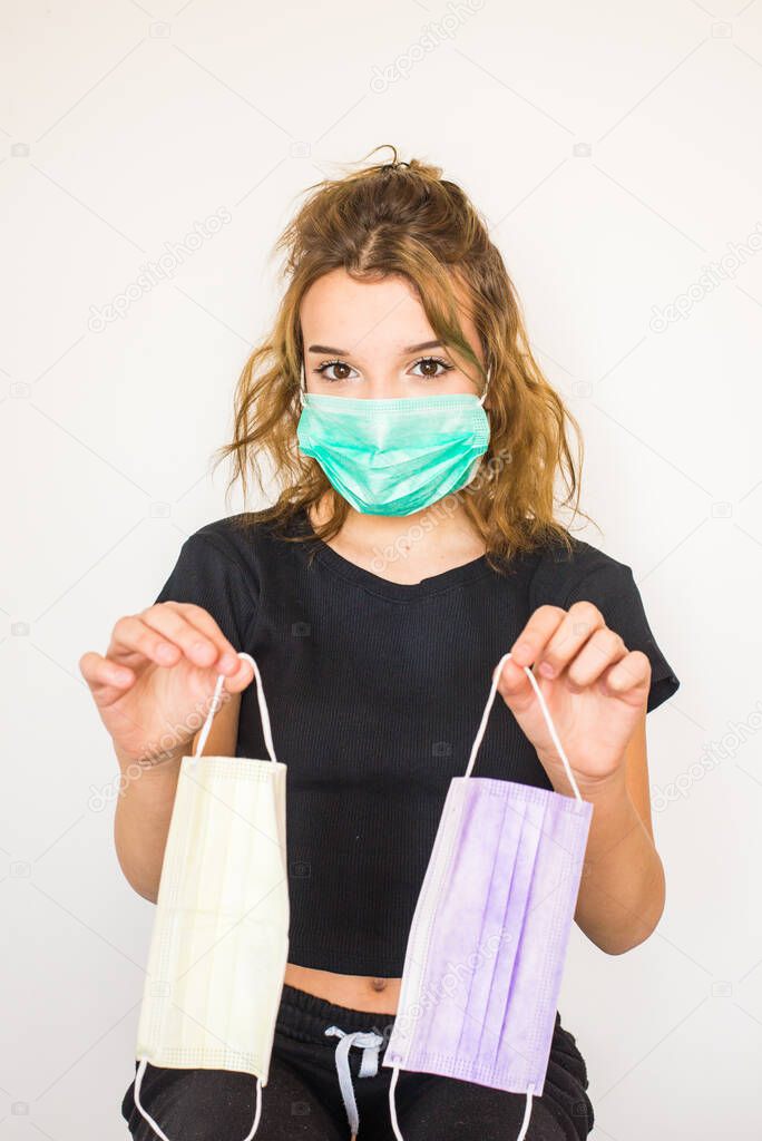 Beautiful teenager brown-eyed girl with brown hair in black top and trousers wearing medical mask lila colour,keeps two coloured protective hygienic masks in hands.Quarantine fashion.Vertical layout.