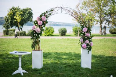 Arka planda göllü ve beyaz masalı pembe taze kesilmiş ortanca ve kremalı güllerle süslenmiş düğün kemerinin güzel görüntüsü
