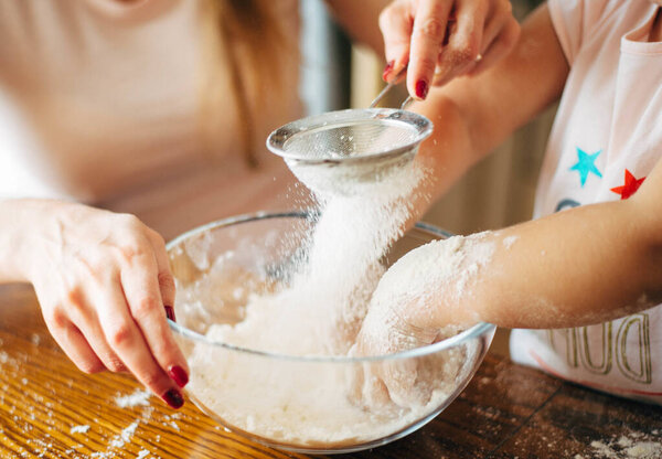 Mother and child sieving flour into a glass bowl. Kid is playing with a flour. Stay home concept. Home activity. Preparing Food with child. Cooking with child at home. Baking with kids Close up