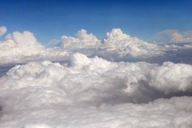 Mavi bir gökyüzü beyaz bulutlar ile üst görünümden bir uçak var. Uçuş bulutların üstünde