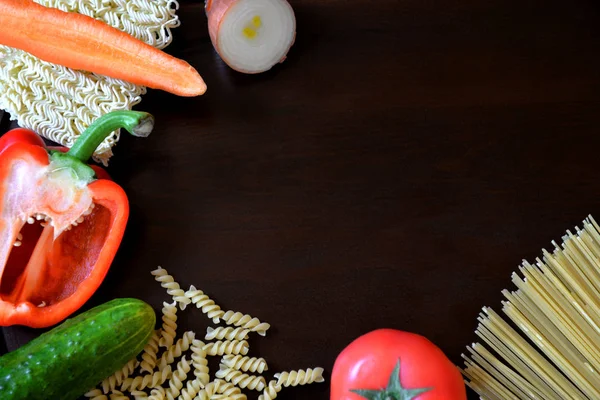 Vegetables and pasta on the left side of the frame. Ingredients on a brown background.