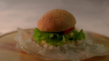 El yapımı sığır eti burger. Gri arka plan üzerinde ahşap bir gemide büyük hamburger biftek pirzola, domates, marul yaprakları ile döner. 