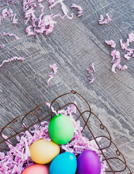 Brightly colored Easter eggs sit in a wire basket, atop a country-style wood floor. This colorful photograph provides a great backdrop and border for your holiday designs.