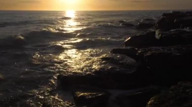 Günbatımında Hazar Denizi. Dalgalar kayalık bir kıyıya vurur.