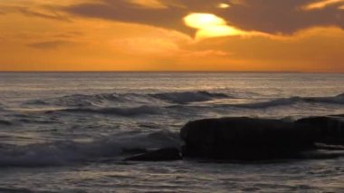 Günbatımında Hazar Denizi. Dalgalar kayalık bir kıyıya vurur.