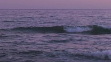 Günbatımında Hazar Denizi. Dalgalar kayalık bir kıyıya vurur.