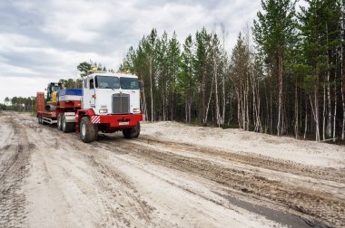 Bir Kenworth C500K traktör kamyonu kazıcı taşır..