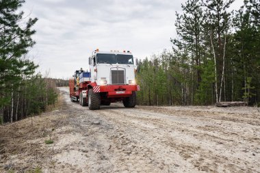 Bir Kenworth C500K traktör kamyonu kazıcı taşır..
