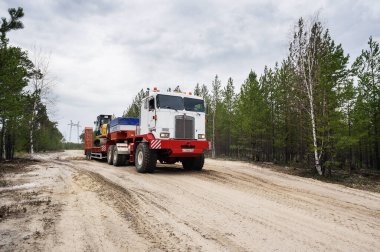 Bir Kenworth C500K traktör kamyonu kazıcı taşır..