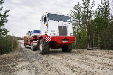 Bir Kenworth C500K traktör kamyonu kazıcı taşır..