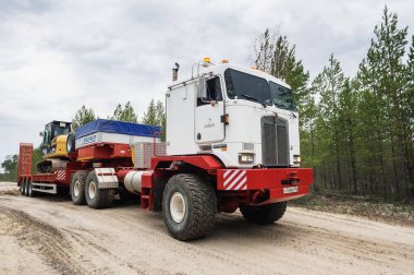 Bir Kenworth C500K traktör kamyonu kazıcı taşır..