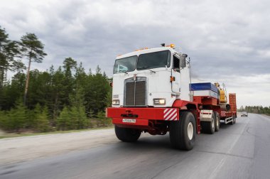 Bir Kenworth C500K traktör kamyonu kazıcı taşır..