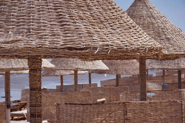 Plage ensoleillée avec palmiers et osier de roseaux parasols sur fond de mer calme et ciel bleu — Photo