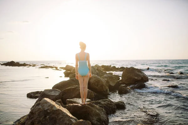 Молодая девушка стоит на камнях в море с красивым закатом — стоковое фото