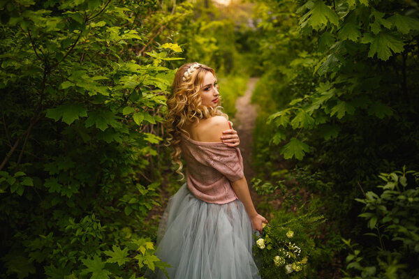 Gorgeous bride in a dress with a wedding bouquet in rustic style enjoying walking in summer or spring forest, back view