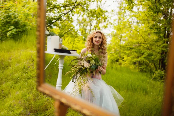 Beautiful bride is sitting outdoors, background with green grass field — Stock Photo, Image