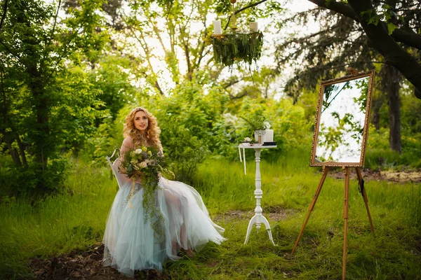 Bride in peignoir with bouquet of hydrangeas sitting in woods — Stock Photo, Image