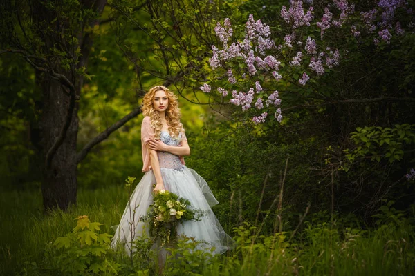Mujer joven guapo en vestido gris sobre fondo de arbustos lila . Imagen De Stock