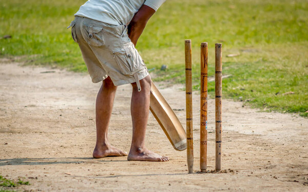 A young Indian boy playing cricket. View of a right handed batsman with all three stumps visible.