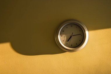 Analogue clock on the yellow wall showing 7:14 time clipart