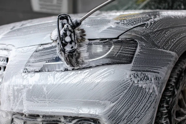 Detalhe sobre a luz dianteira do carro que está sendo lavada com espuma de sabão — Fotografia de Stock