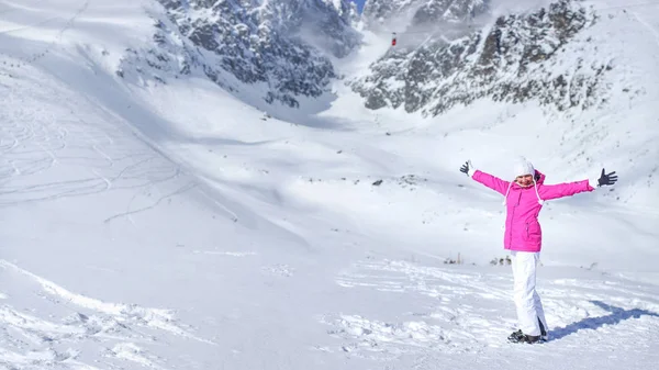 Счастливая молодая женщина в розовой лыжной куртке, перчатках, шляпе и лыжных ботинках — стоковое фото