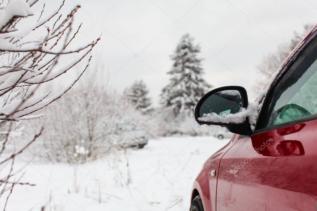 Detail on mirror of red car parked on a winter road with snow co