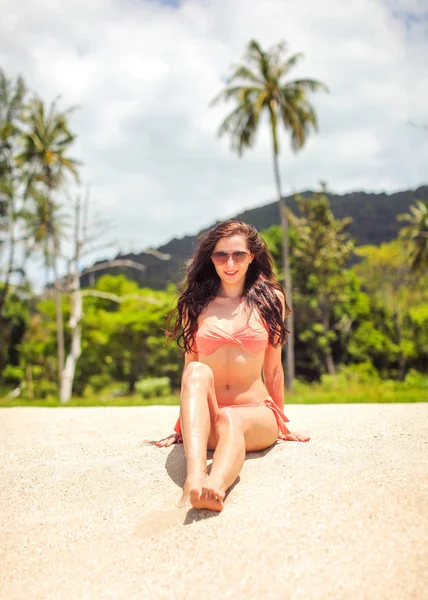 Young woman in red bikini sitting on the fine sand beach with pa — Stock Photo, Image