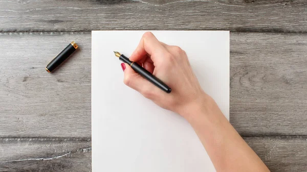 Mano de mujer sosteniendo pluma negra lista para escribir en blanco —  Fotos de Stock